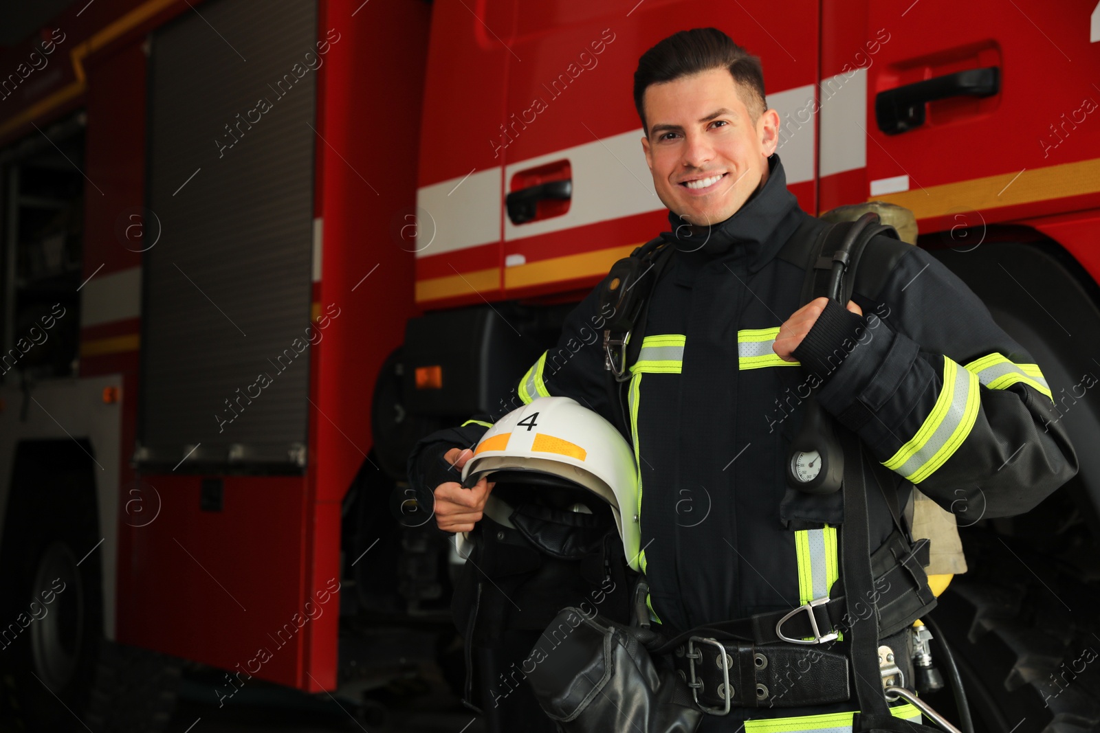 Photo of Portrait of firefighter in uniform with helmet near fire truck at station, space for text