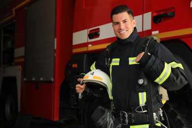 Photo of Portrait of firefighter in uniform with helmet near fire truck at station, space for text