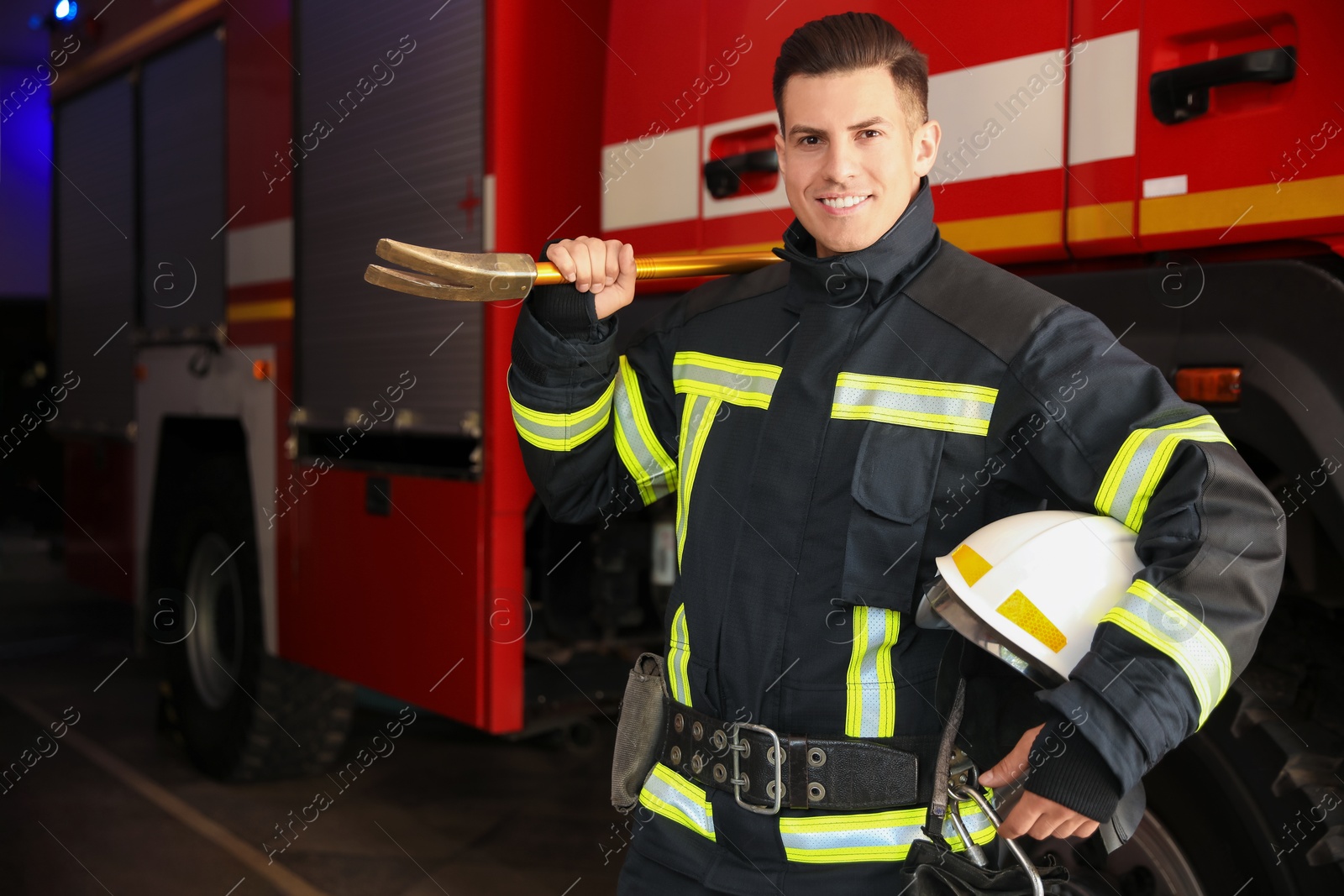 Photo of Portrait of firefighter in uniform with helmet and entry tool near fire truck at station, space for text