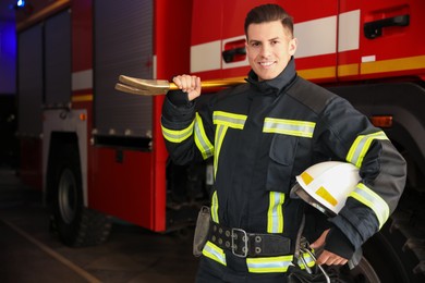 Portrait of firefighter in uniform with helmet and entry tool near fire truck at station, space for text