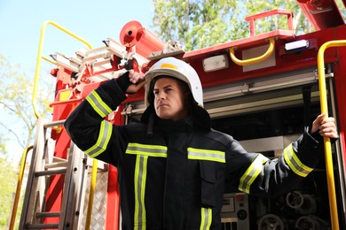 Photo of Portrait of firefighter in uniform and helmet near fire truck outdoors