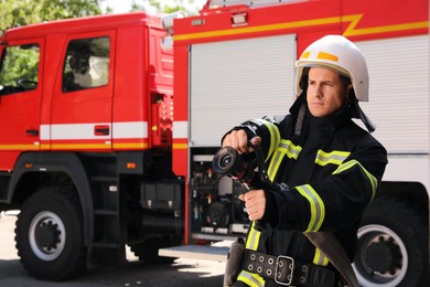 Photo of Firefighter in uniform with high pressure water jet near fire truck outdoors