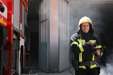 Photo of Portrait of firefighter in uniform with high pressure water jet near fire truck outdoors