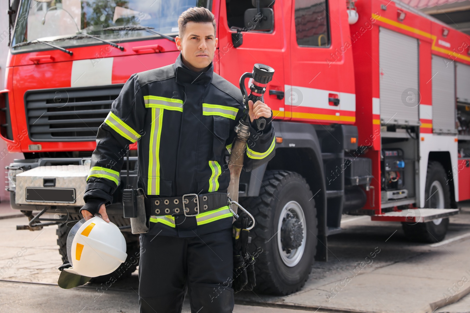 Photo of Portrait of firefighter in uniform with high pressure water jet near fire truck outdoors