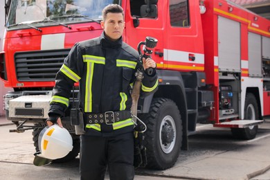 Portrait of firefighter in uniform with high pressure water jet near fire truck outdoors