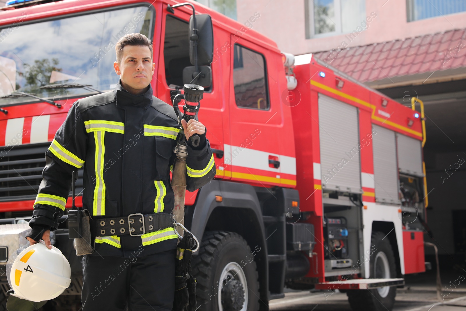 Photo of Portrait of firefighter in uniform with high pressure water jet near fire truck outdoors