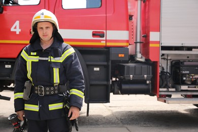 Portrait of firefighter in uniform and helmet near fire truck outdoors