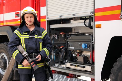 Portrait of firefighter in uniform with high pressure water jet near fire truck outdoors