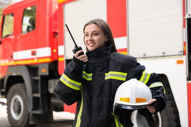 Firefighter in uniform using portable radio set near fire truck outdoors