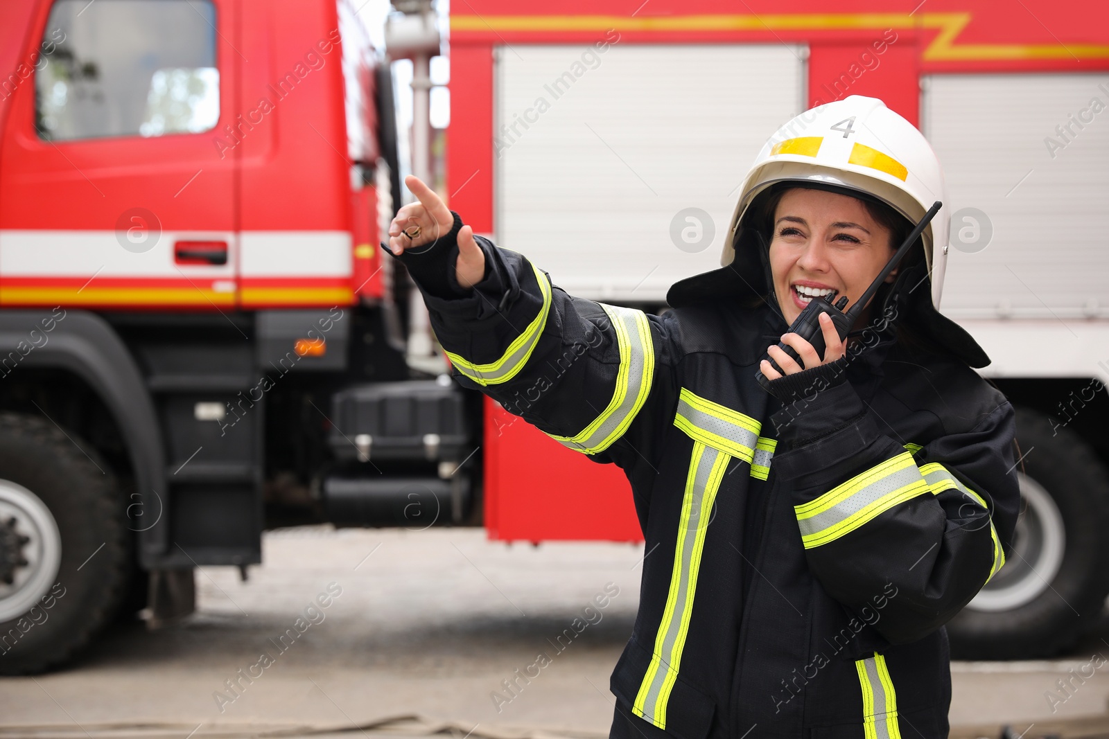 Photo of Firefighter in uniform using portable radio set near fire truck outdoors