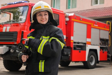 Firefighter in uniform with high pressure water jet near fire truck outdoors