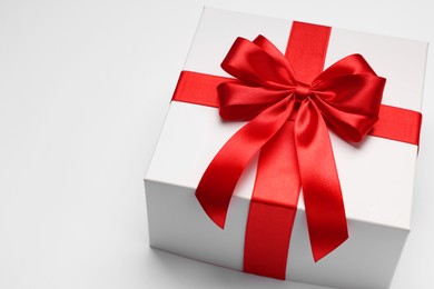 Photo of Gift box with red bow on light grey background, closeup. Space for text