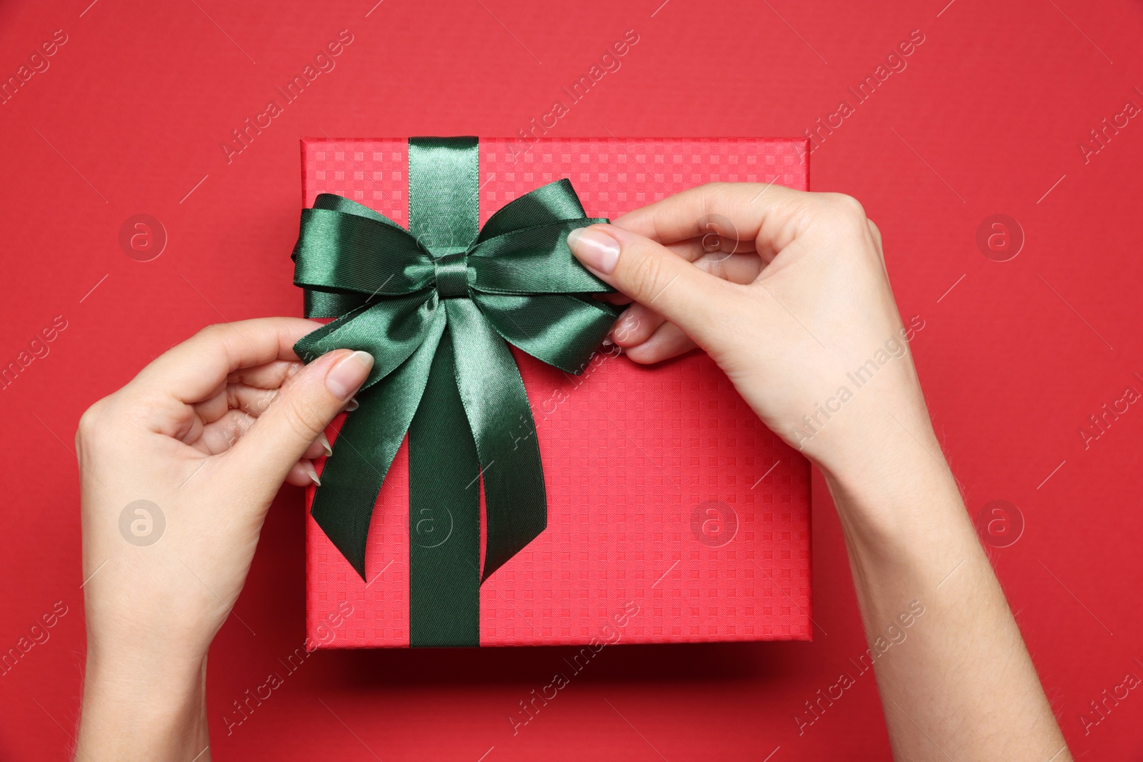 Photo of Woman decorating gift box with bow on red background, top view