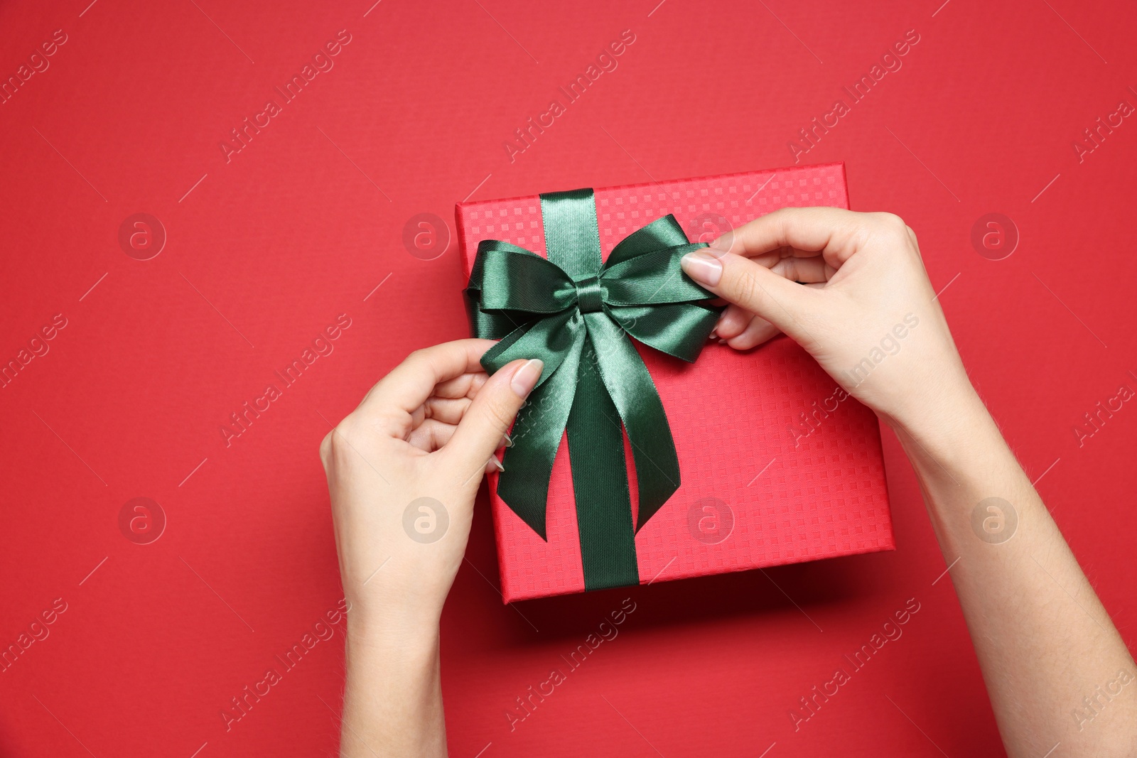 Photo of Woman decorating gift box with bow on red background, top view