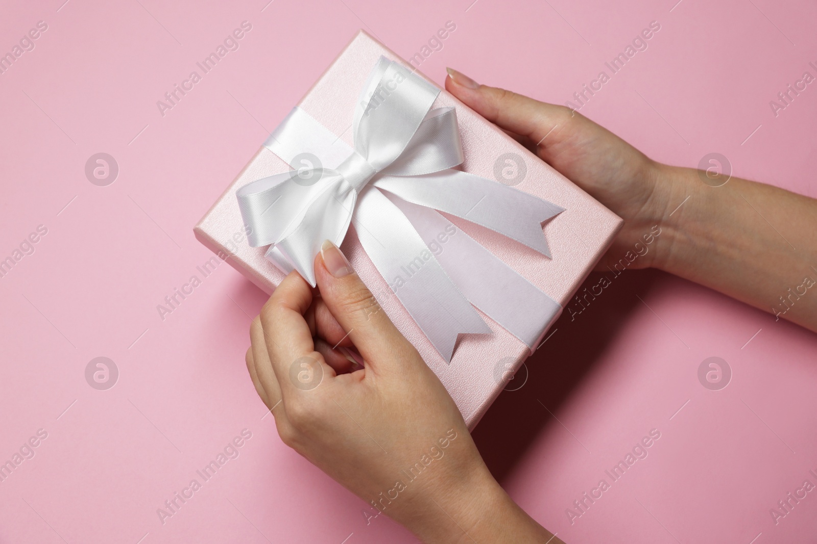 Photo of Woman decorating gift box with bow on pink background, top view