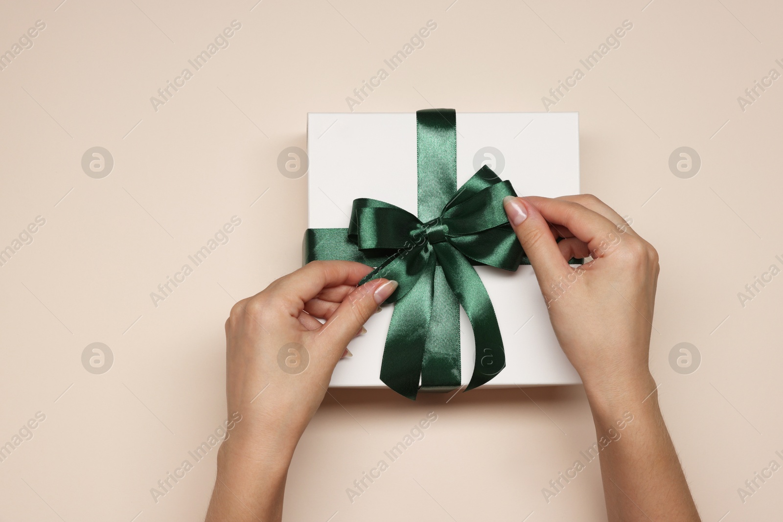 Photo of Woman decorating gift box with bow on beige background, top view