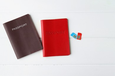 Passports and SIM cards on white wooden table, flat lay