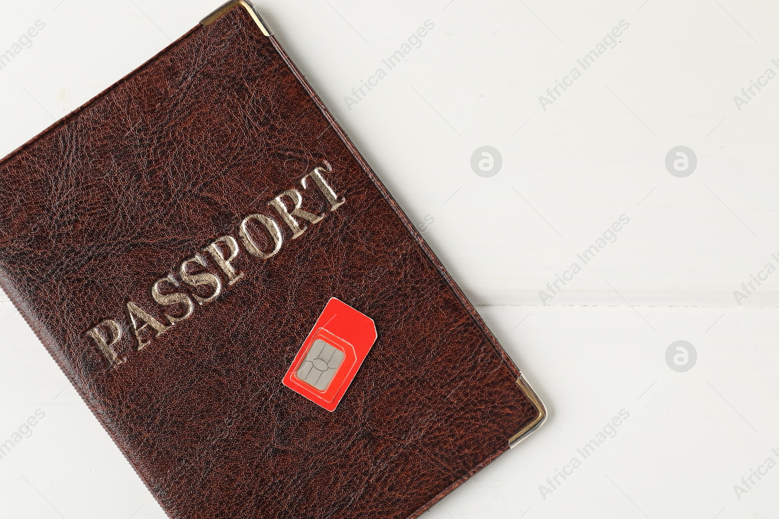 Photo of Passport and SIM card on white wooden table, top view. Space for text