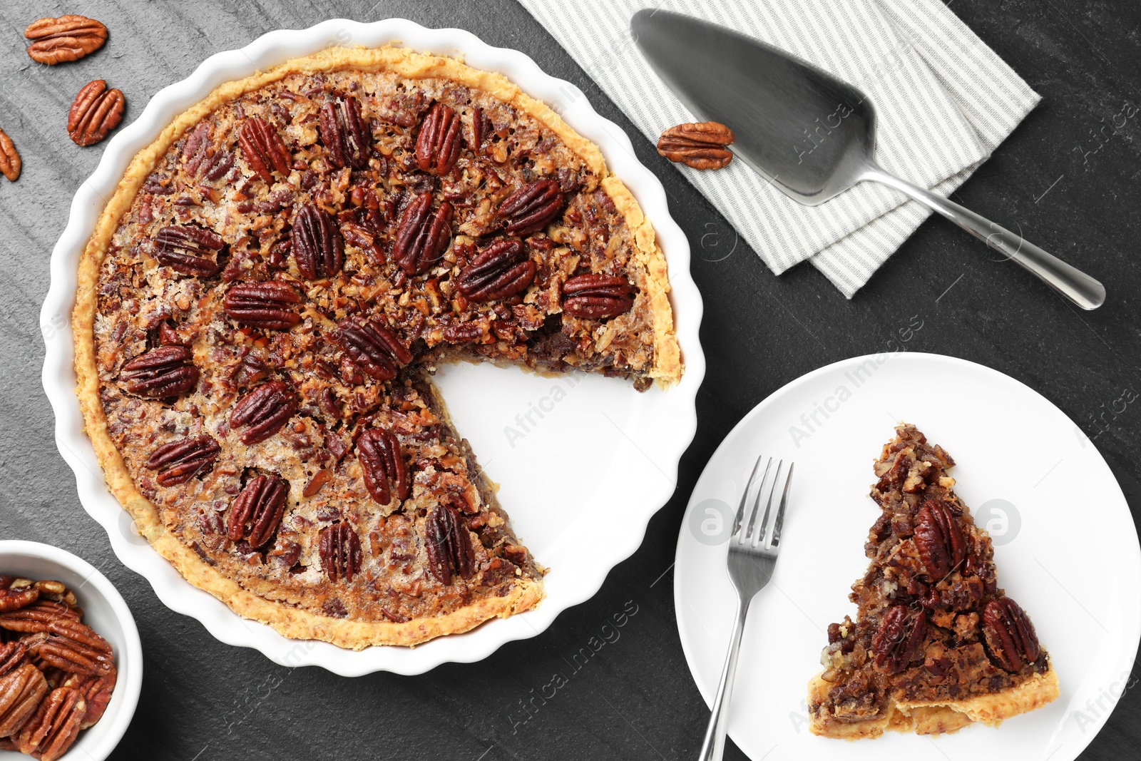 Photo of Delicious pecan pie, fresh nuts and cake server on dark gray textured table, top view