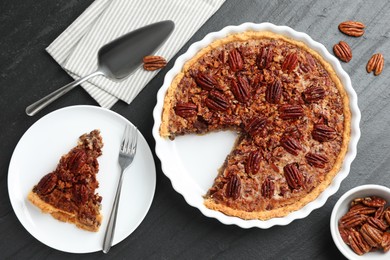 Photo of Delicious pecan pie, fresh nuts and cake server on dark gray textured table, top view