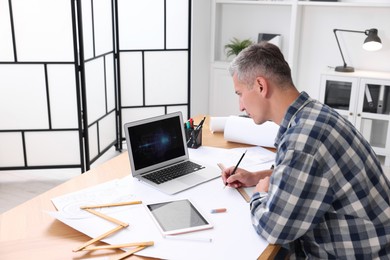 Photo of Architect making engineering drawing at wooden table in office