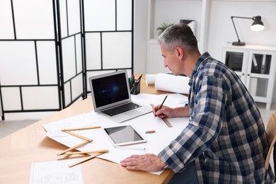 Photo of Architect making engineering drawing at wooden table in office