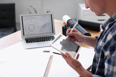 Architect making digital engineering drawing on tablet at table in office, closeup