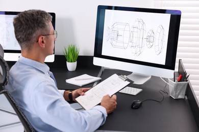 Photo of Architect checking engineering drawing at table in office