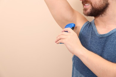 Smiling man applying solid deodorant on beige background, closeup. Space for text