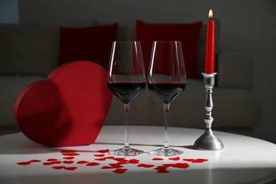 Burning candle, wine in glasses and paper hearts on table indoors