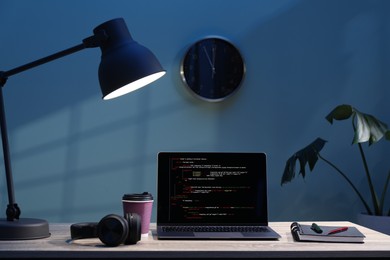 Photo of Programmer's workplace. Modern laptop with unfinished code, headphones and other supplies on wooden desk indoors