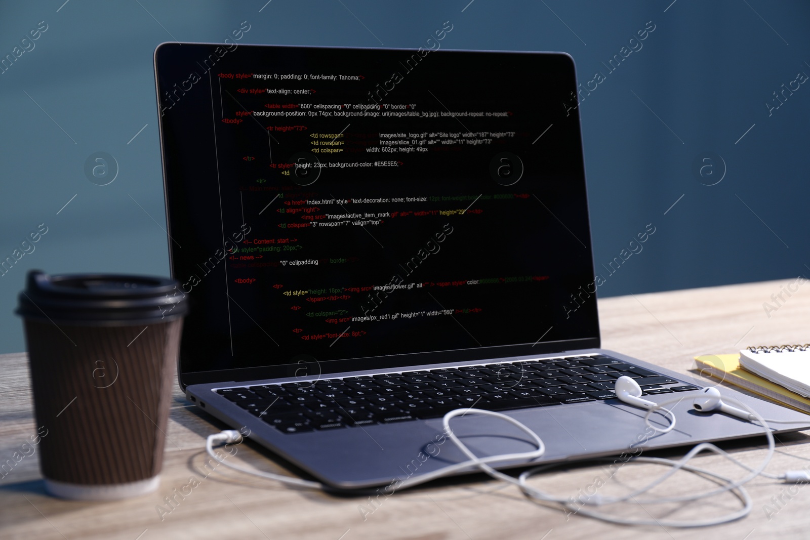 Photo of Programmer's workplace. Modern laptop with unfinished code, earphones and paper cup of drink on wooden desk