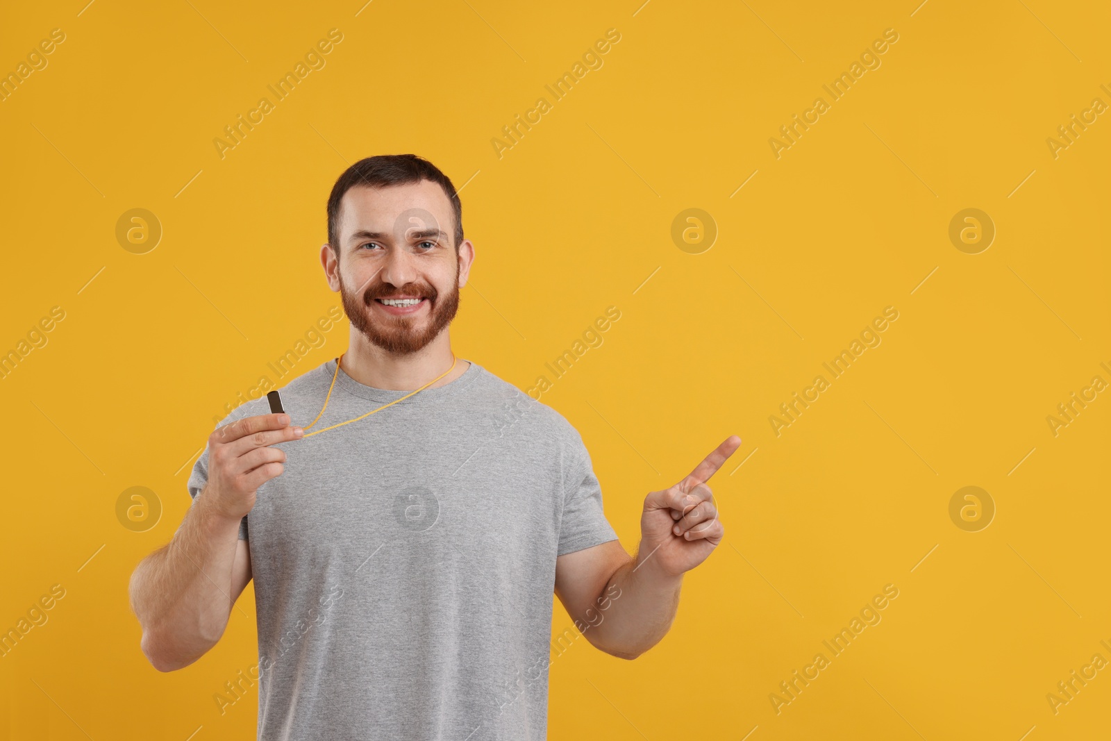 Photo of Happy young man with whistle on orange background, space for text