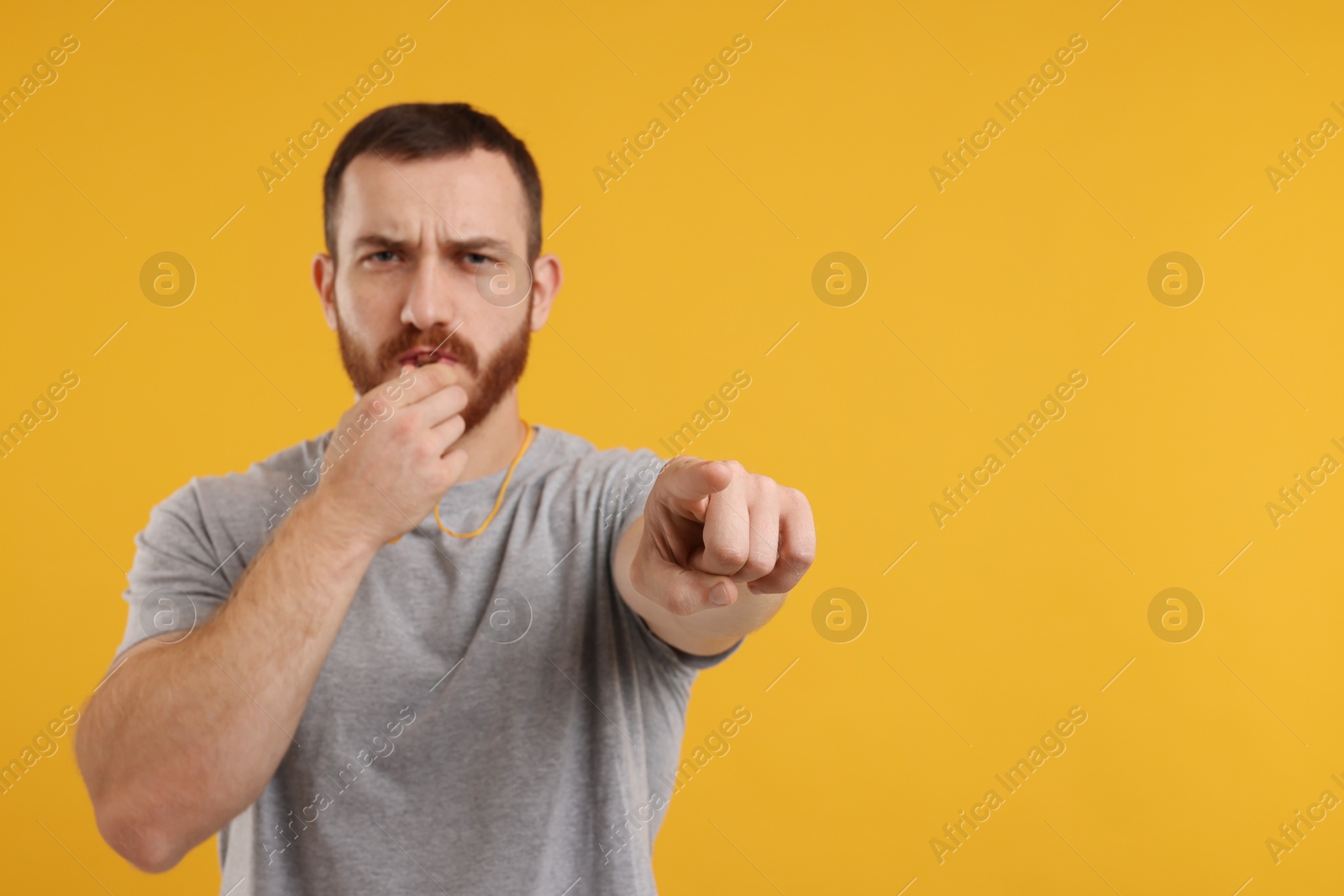 Photo of Young man blowing whistle on orange background, space for text