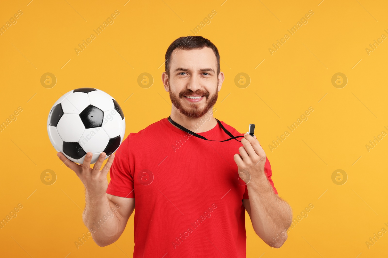 Photo of Happy young man with whistle and soccer ball on orange background