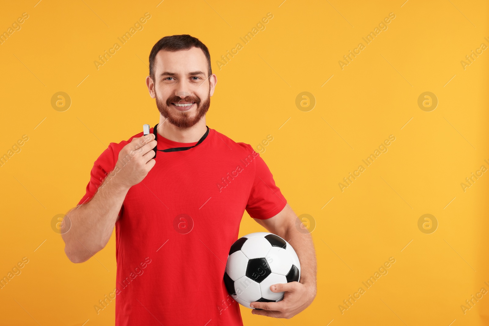 Photo of Happy young man with whistle on orange background, space for text