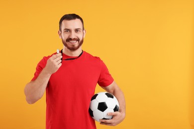 Photo of Happy young man with whistle on orange background, space for text