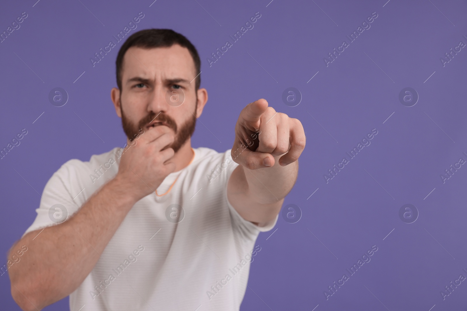 Photo of Young man blowing whistle on purple background, space for text