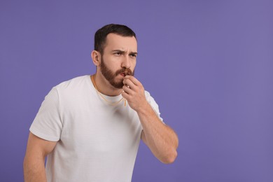 Young man blowing whistle on purple background, space for text