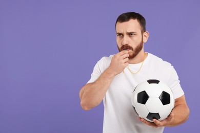 Photo of Young man with soccer ball blowing whistle on purple background, space for text