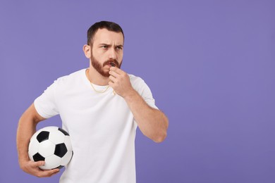 Photo of Young man with soccer ball blowing whistle on purple background, space for text