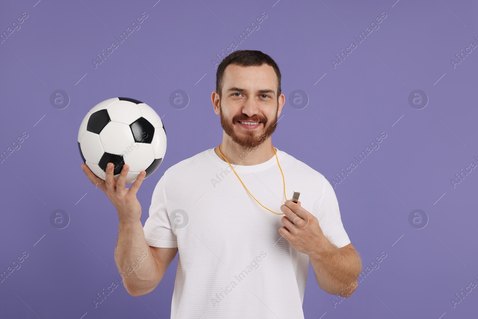 Photo of Happy young man with whistle and soccer ball on purple background