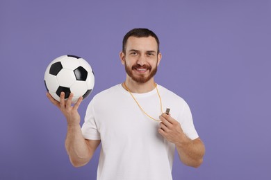 Happy young man with whistle and soccer ball on purple background