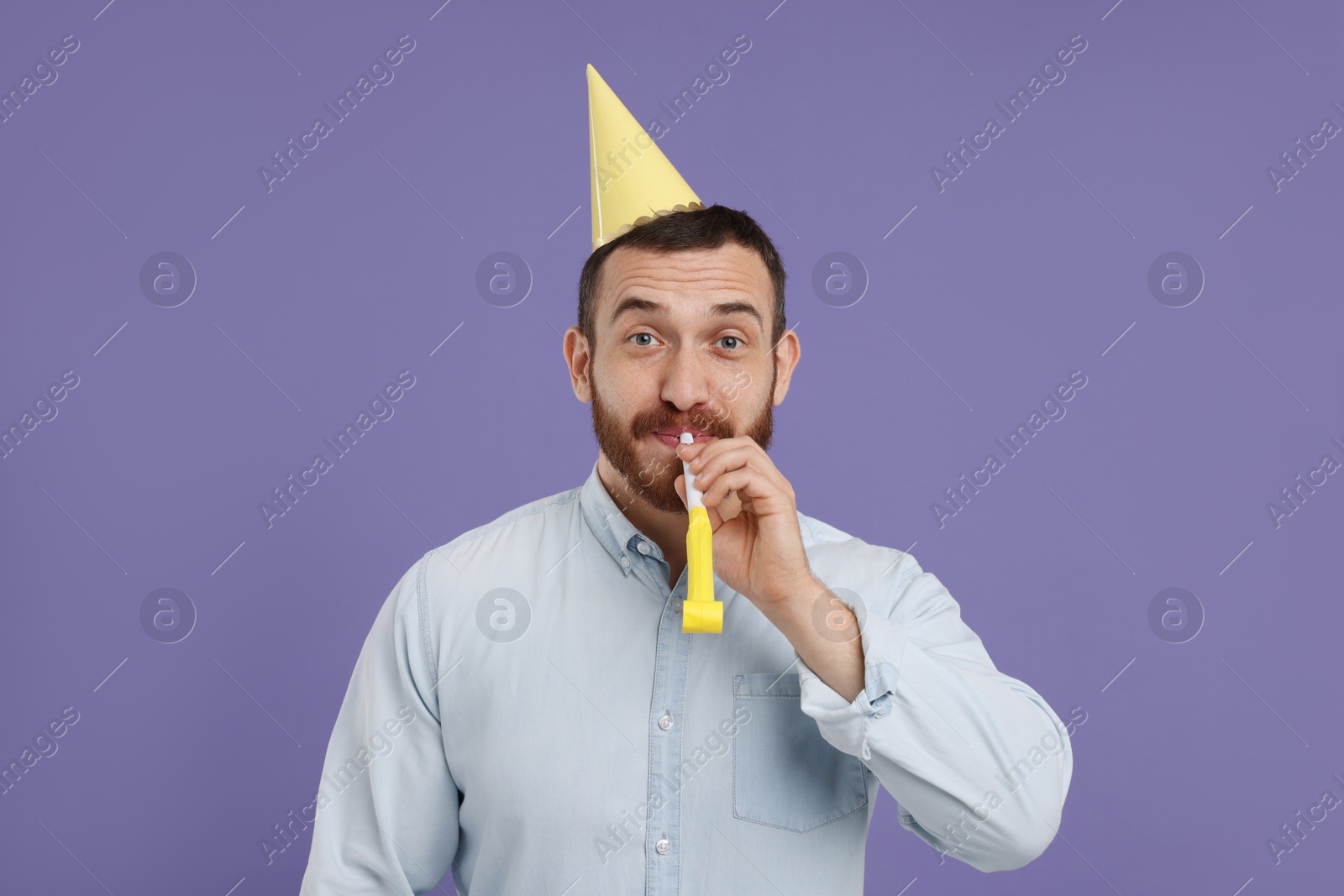 Photo of Man in party hat with blower on purple background