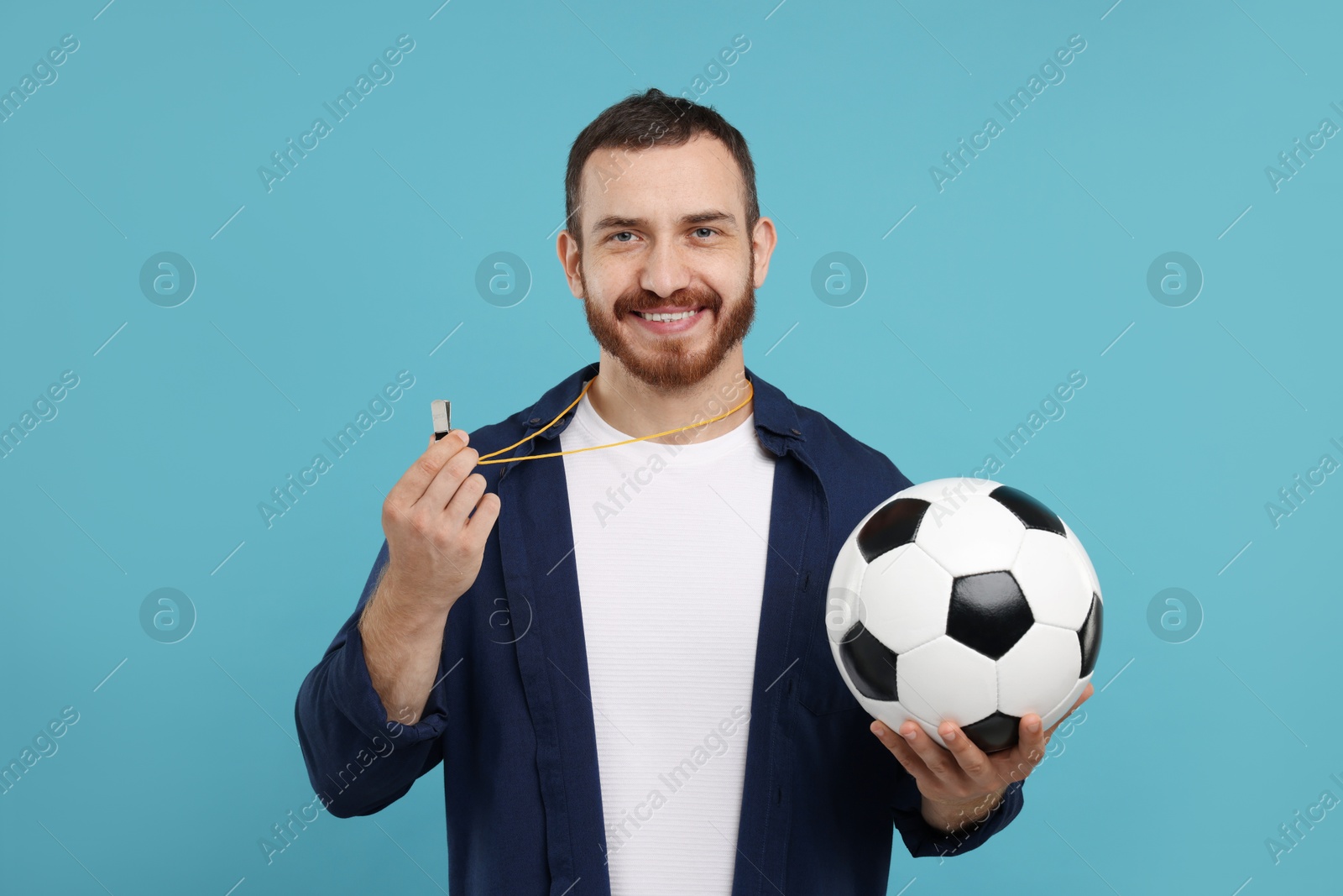 Photo of Happy young man with whistle and soccer ball on light blue background