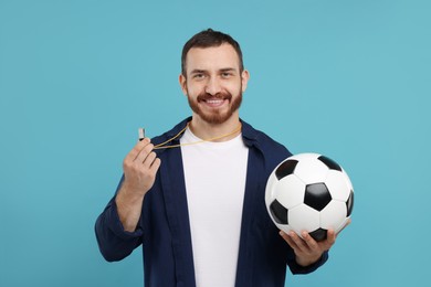 Happy young man with whistle and soccer ball on light blue background