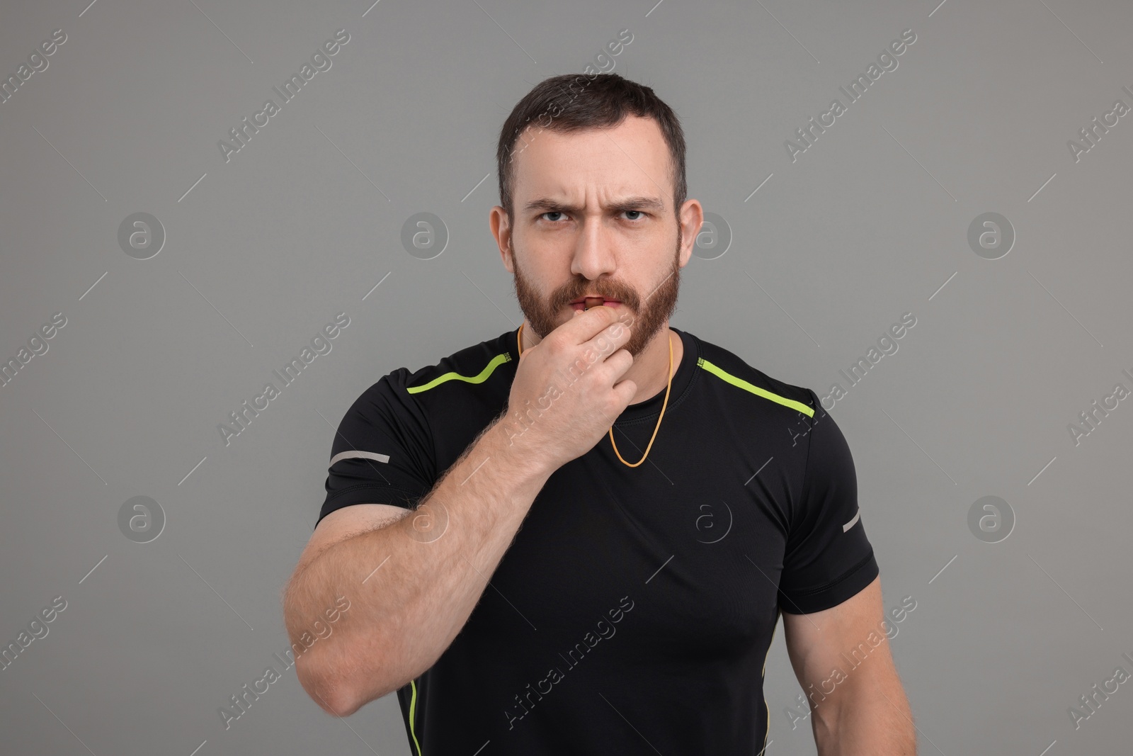 Photo of Young man blowing whistle on grey background