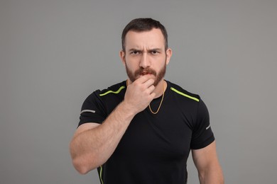 Young man blowing whistle on grey background