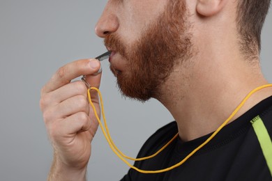 Photo of Man blowing whistle on grey background, closeup