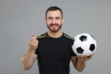 Photo of Happy young man with whistle and soccer ball on grey background